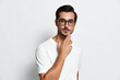 © SHOTPRIME STUDIO - Thoughtful young man wearing glasses, posing confidently with hand on chin, isolated on plain solid background. Modern lifestyle and self-reflection concept.
