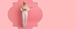 © Prostock-studio - A woman smiles and gestures with her hand while standing against a solid pink background. She wears a light sweater, white pants, and a hijab. The composition focuses on her cheerful expression.