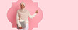 © Prostock-studio - A woman wearing a headscarf stands in a pink background. She is smiling and pointing to her side while holding a laptop. The scene captures a moment of engagement and purpose.