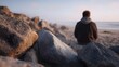 © Thares2020 - A solitary person sits on rocks by the ocean at dawn contemplating the tranquil horizon