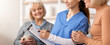 © Prostock-studio - A caregiver meets two elderly women in a home setting. The caregiver holds a clipboard and listens attentively as the women chat. The scene shows a friendly interaction during a health check.