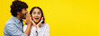 © Prostock-studio - Two people are having a joyful moment together. One person whispers to the other, who shows excitement and surprise. They are in front of a bright yellow background.