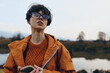 © SHOTPRIME STUDIO - Young woman lifestyle outdoors wearing orange jacket and sweater holds smartphone, looks away with sunglasses. Autumn nature background with lake and trees. Casual fashion and technology concept.