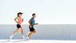 © muse studio - Active man and woman jogging side by side outdoors on a bright day with a clean background