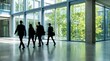 © Nest - Silhouetted business people walk purposefully across a brightly lit, spacious modern office lobby with large windows looking onto green trees.