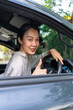 © BJ Day Stock - Happy Asian woman sitting in the driver's seat of a car showing a thumbs-up gesture and smiling at the camera, representing safe driving, car insurance, or buying a new auto. Vertical Shot