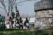 © qunica.com - Paintball team in camouflage, masks, and gear pose with rifles in an outdoor obstacle field.