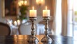 © Agusstudio - A pair of ornate silver candlesticks holding flickering lit white candles on a polished table, creating a warm and elegant ambiance within a sophisticated interior.