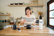 © Stella 16 - Young Asian woman carefully scooping matcha powder into a traditional tea bowl in a calm and minimalist kitchen setting