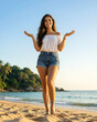© Aleksei Solovev - Woman with long brown hair wearing a white off-the-shoulder top and blue denim shorts standing on a sandy beach with palm trees and ocean in the background, exuding happiness.