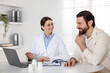 © New Africa - Man having appointment with doctor at white desk in clinic