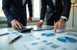 © Raisa - Two men in suits review financial charts and graphs on a desk. One uses a calculator, the other points to data on a tablet. Teamwork planning business growth with analytics.