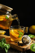 © Pixel-Shot - Pouring of tasty fruit tea from glass teapot into cup on black grunge table, closeup
