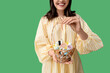 © Pixel-Shot - Young woman holding Easter basket with cosmetic products on green background
