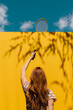 © Westend61 - Woman holding badminton racket over yellow wall during sunny day