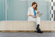 © Westend61 - Businesswoman in white pant suit, sitting on bench, using laptop