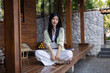 © Jirapaporn - Young woman sitting cross-legged on wooden porch