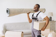 © anatoliycherkas - Mover carrying rolled carpet and box during residential relocation, happy professional delivering household items