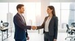 © Chenda - A man and a woman are shaking hands in a modern office setting. They are both dressed in professional attire, consisting of suits and blazers.