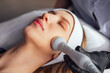 © Dasha Petrenko - Young woman receiving facial treatment in a spa setting, with a beauty technician using a device on her skin, showcasing relaxation and skincare techniques for rejuvenation