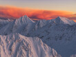 © AmazingAerialAgency - Aerial view of snow-capped peaks pierce the sky as the sun paints the clouds in fiery hues of orange and pink, Lyngen, Troms, Norway.