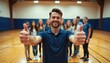 © Viktor - Smiling man gives thumbs up gesture in gym with students behind. Teacher expresses approval and positivity for youth sports team success and teamwork.