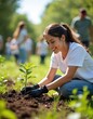 © Viktor - Young woman plants small tree in soil wearing gloves. People help in background on sunny day for eco project. Teamwork for nature care and green growth.