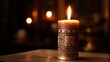 © Honey - A lit candle with an ornate design sits on a table in a dark room with other candles in the background.