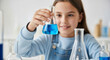© imagemir - Young Girl Conducts an Experiment, Holding a Blue Liquid in a Flask, Showcasing Curiosity and Enthusiasm for Science Highlighting a Learning and Education Concept