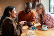 © Marko Geber - Three friends laughing over smartphone at cafe
