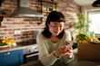 © Davor - Smiling woman using smartphone in home kitchen with fresh grocery delivery