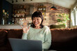 © Davor - Smiling woman waving during video call at home