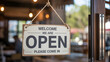© Khan - A rustic Welcome We Are Open sign hangs on a bright glass shop door inviting customers during a sunn