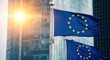 © bik - European flags waving in front of a modern glass building at sunrise