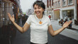 © Krakenimages.com - Young woman smiling with orange pendant necklace and open arms gesture on a busy city street with storefronts and scooters; joy welcome.