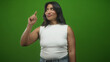 © Krakenimages.com - Woman pointing index finger downward while looking at it, wearing white sleeveless top and jeans in a green studio backdrop; playful curiosity.