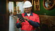 © Krakenimages.com - Man construction worker in white hard hat and red jacket taps tablet with hand inside building; efficiency confidence.
