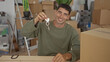 © Krakenimages.com - Man holds key ring while pointing finger to shiny house keys amidst stacked moving boxes in building; fresh start excitement.
