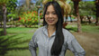 © Krakenimages.com - Young chinese woman smiling outdoors in a vibrant green park setting with trees and flowers in the background, exuding a sense of joy and tranquility.