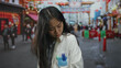 © Krakenimages.com - Chinese woman scientist in a uniform standing outdoors on a busy street, looking concerned and holding her shoulder with colorful shops in the background.