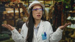 © Krakenimages.com - Chinese woman in hardhat and lab coat stands confused in clothing store facing camera indoors.