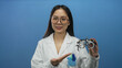 © Krakenimages.com - Woman optician in lab coat holds glasses against blue background demonstrating professional equipment in a clinical setting