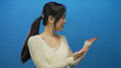© Krakenimages.com - Young woman presenting against a vibrant blue background with both hands extended slightly to the side, emphasizing her cheerful expression and inviting gesture.