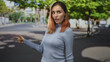 © Krakenimages.com - Redhead young woman smiling and giving thumbs up with bare hand on a tree-lined street crosswalk, wearing a ribbed blue turtleneck sweater; approval encouragement warmth.