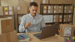 © Krakenimages.com - Man holding glasses rubs eyes at workstation inside a warehouse building amid stacked boxes and laptop; work fatigue.