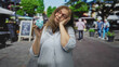 © Krakenimages.com - Woman holding blue piggy bank in hand, glasses lifted and head tilted in a busy street market; financial concern retirement.