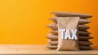 © Fahad - A stack of brown envelopes with one labeled TAX sits on a wooden table against an orange background.