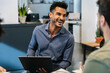 © Xavier Lorenzo - Smiling corporate employee with laptop engaging in a positive discussion with colleagues, expressing happiness and collaboration in a modern office setup