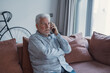 © Daniel - Worried concerned senior elder man talking on cellphone to doctor, feeling unwell, calling for emergency, ambulance, sitting on sofa at home, contact helpline, using mobile phone 