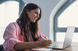 © Daniel - Focused woman housewife seated at table writing down useful information, phone number or address of services founded in internet, groceries shopping list, do routine home work using personal organizer